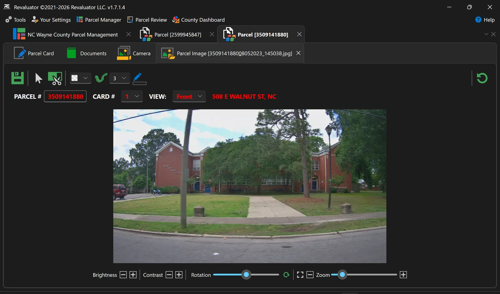 Image editor showing a street-level still of a brick house with brightness, contrast, rotation and zoom controls beneath it.